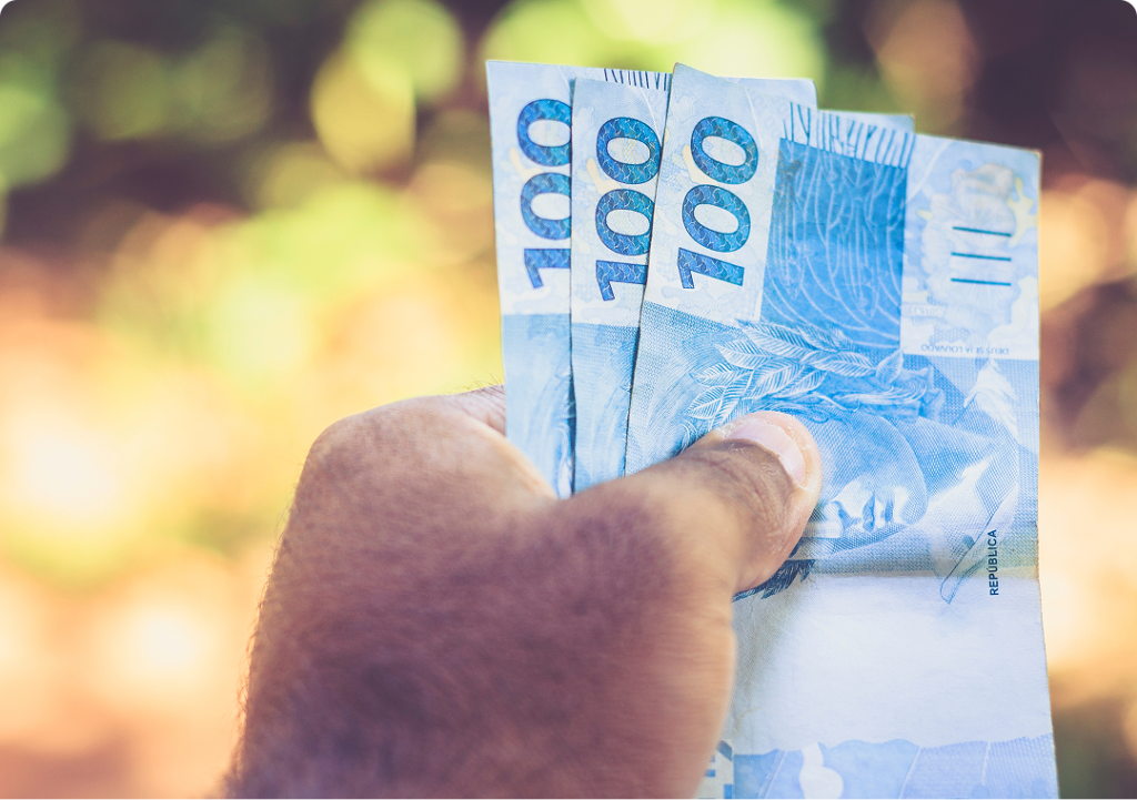 mão segurando notas de cem reais