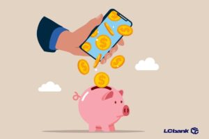 "Mão usando celular para depositar moedas em um cofrinho rosa, representando antecipação de valores pelo LCbank.